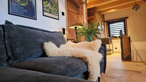 Ein gemütliches Wohnzimmer mit einem grauen Sofa, einer flauschigen weißen Decke und einem Blumentopf.