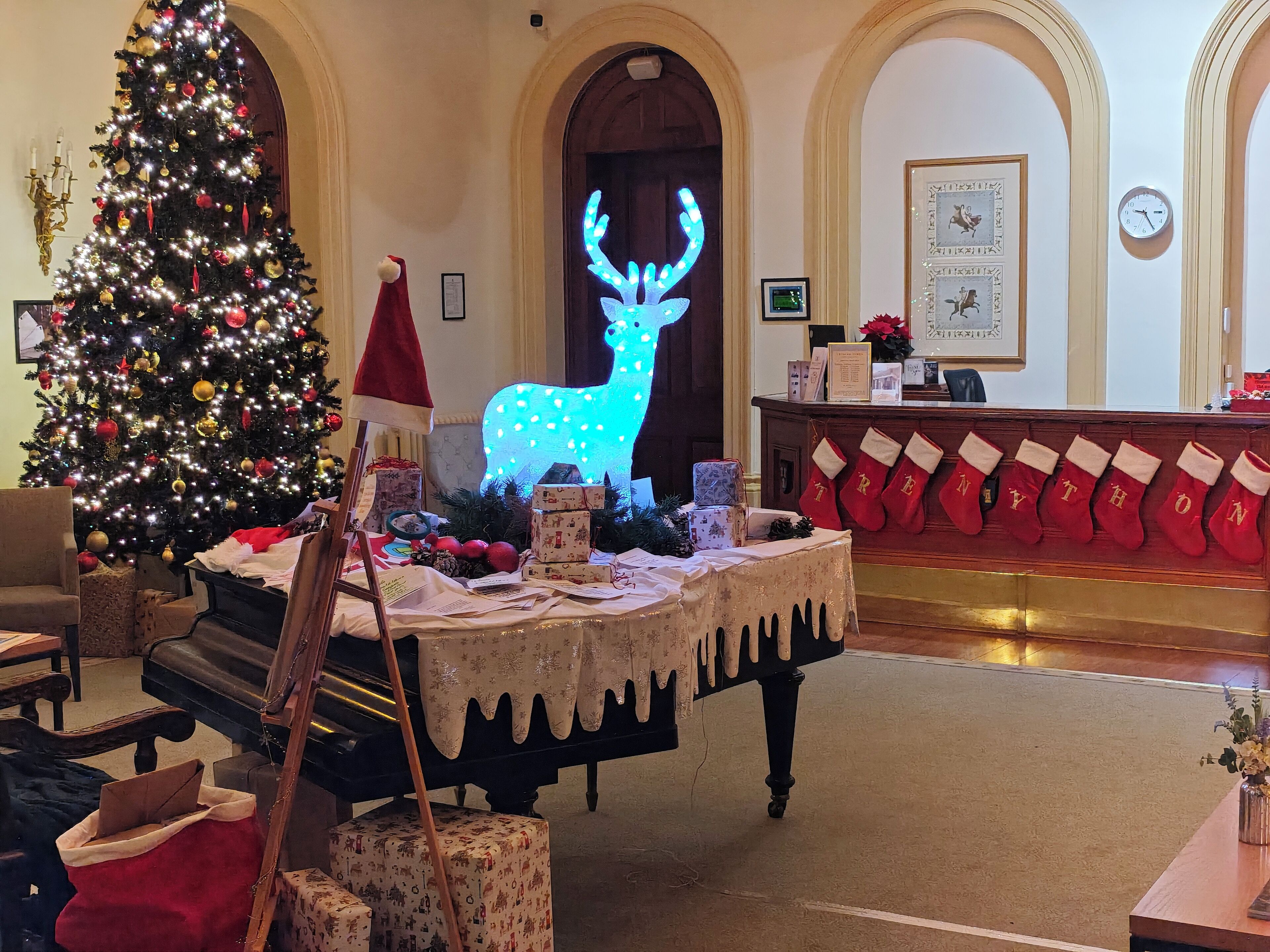 A lobby with a Christmas tree, a piano, a reception desk, and a clock on the wall.