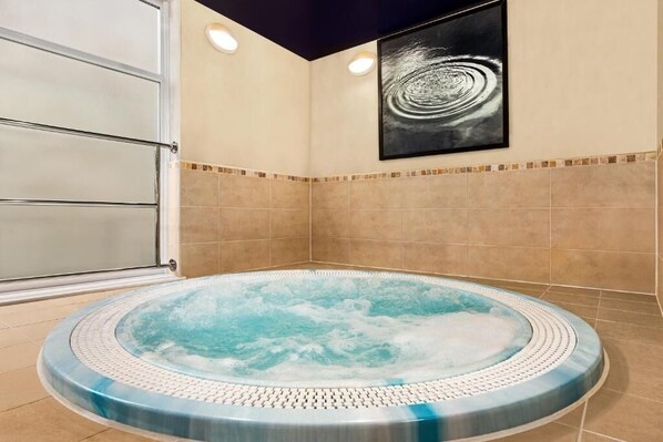 A hot tub in a corner with a tiled wall and a framed artwork above it.