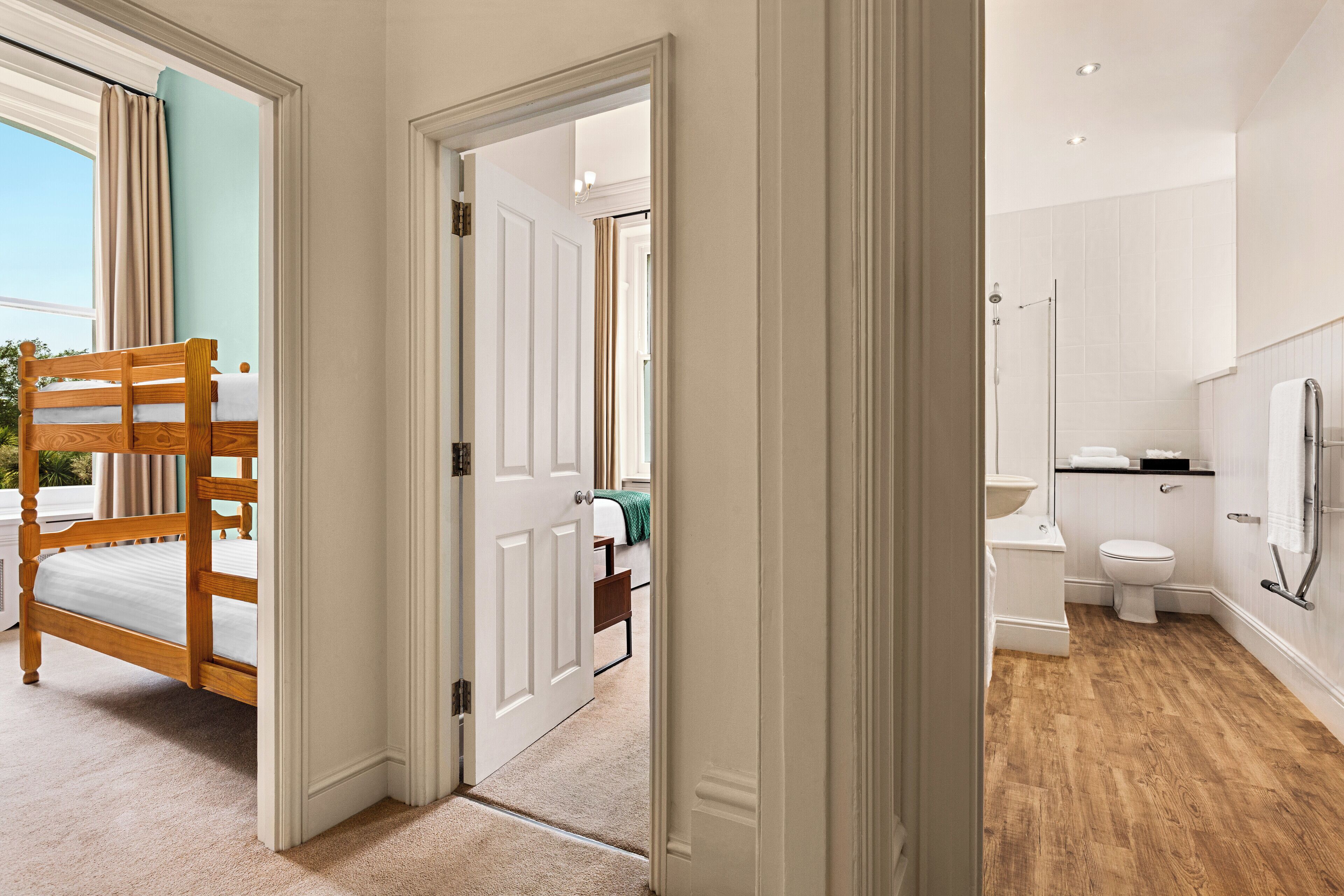 A bedroom with a wooden bunk bed, a bathroom with a toilet and bathtub, and a view of the outdoors through a window.