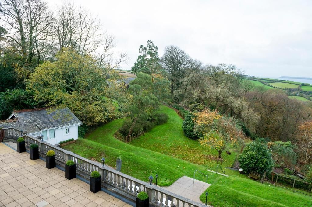 A landscaped garden with a white building, a stone pathway, and a view of the countryside.