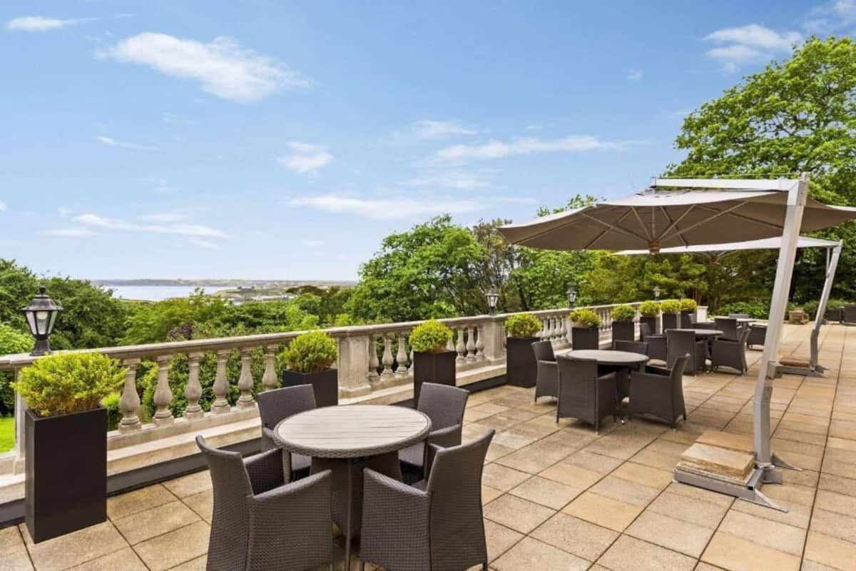 An outdoor patio with round tables and chairs, a pergola with a canopy, and a view of the sea.