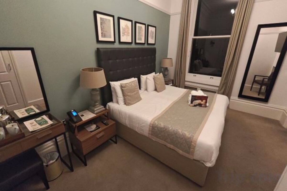 A hotel room with a bed, bedside tables, a desk, and a large window.