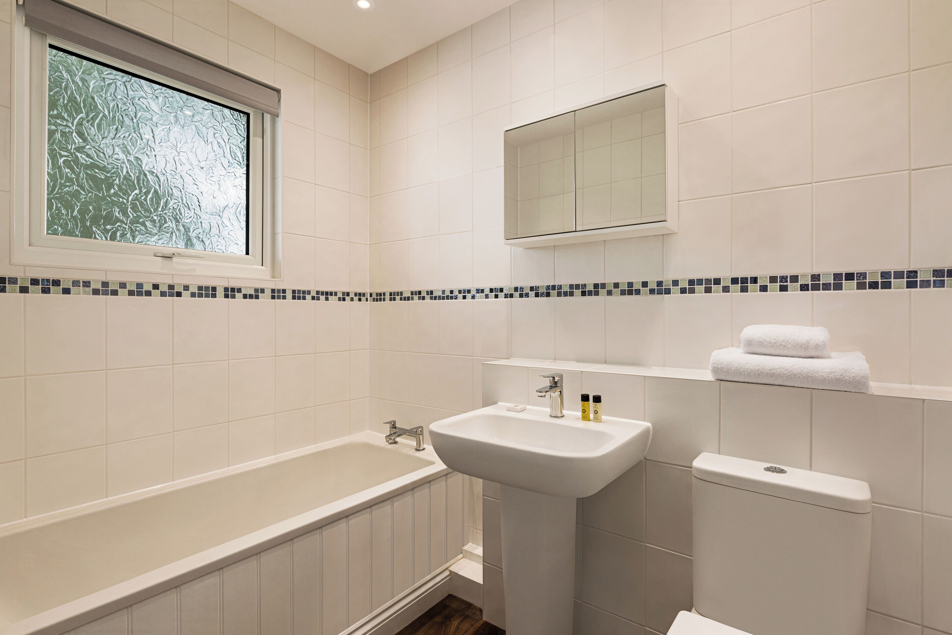 Ein Badezimmer mit Badewanne, Waschbecken, Toilette und einem Fenster mit Blick auf Bäume.