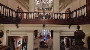 A grand staircase with ornate railings, a chandelier, and a view of the lobby area.