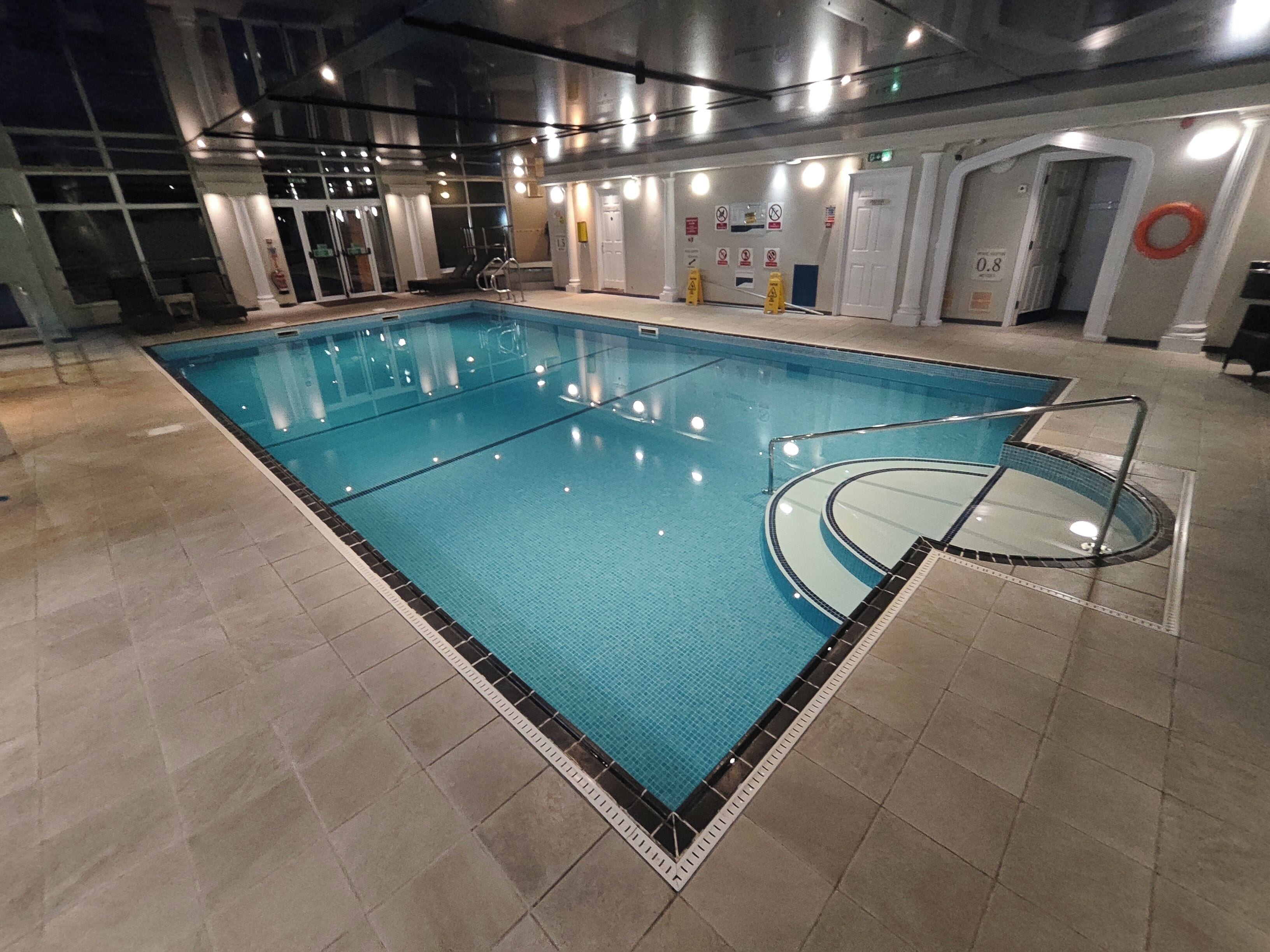 An indoor swimming pool with clear water, tiled floor, and a safety ladder.