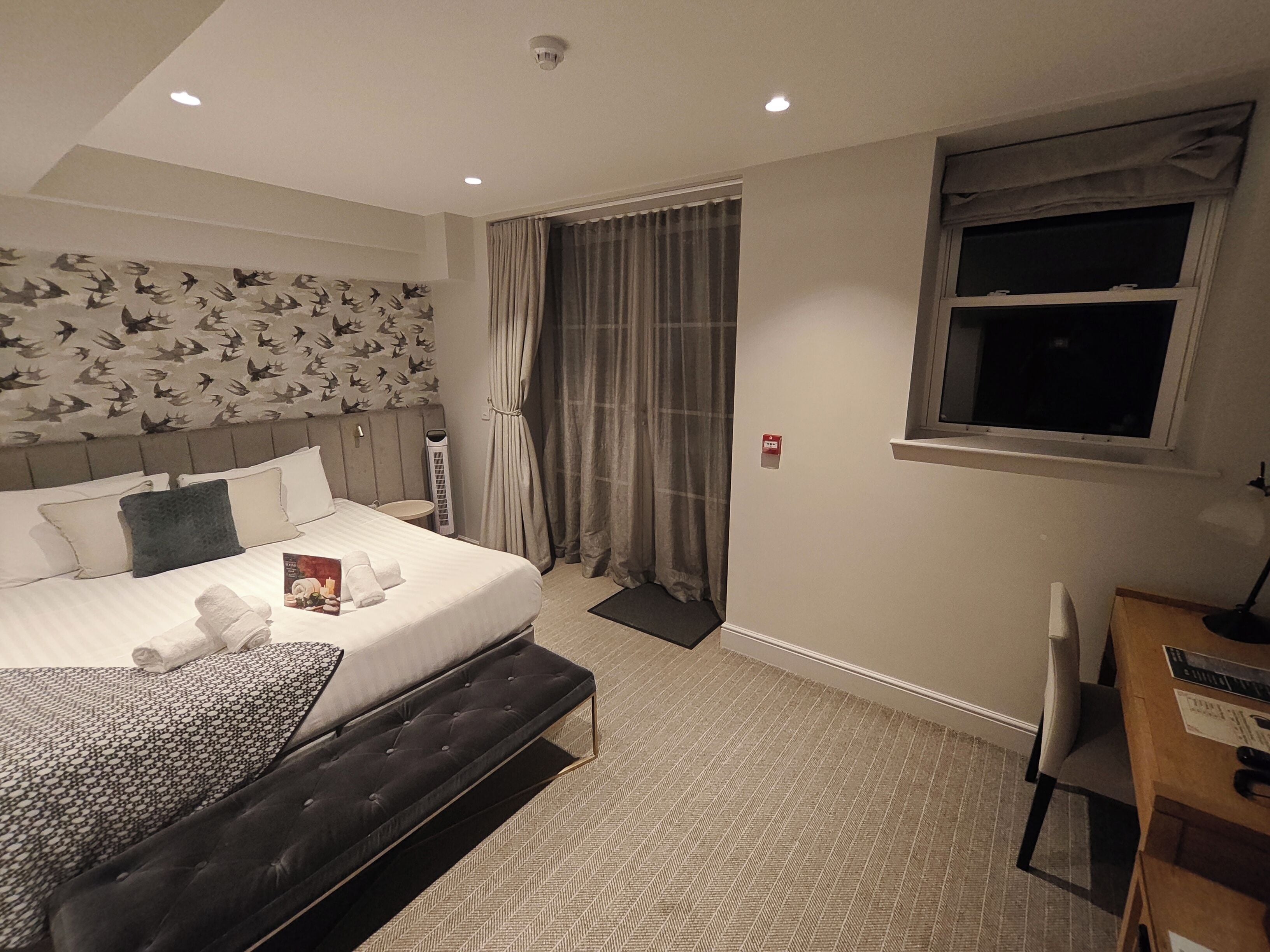 A hotel room with a large bed, a desk, and a window.