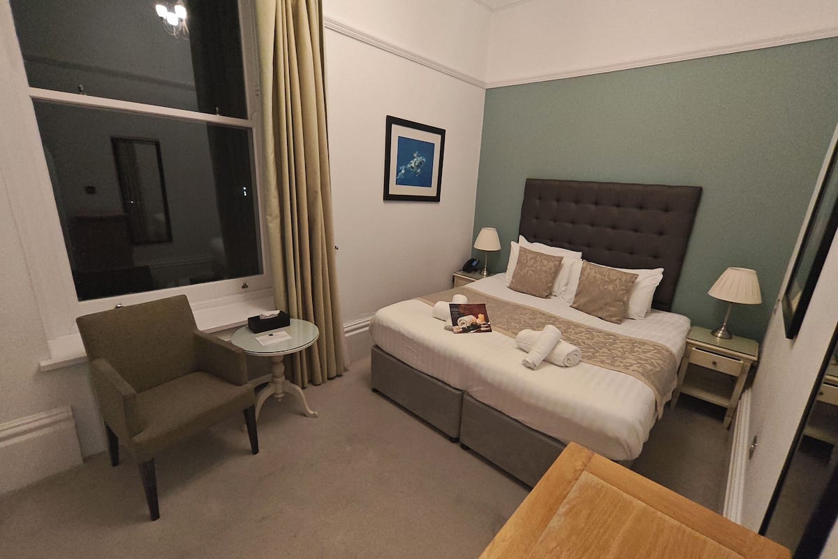 A hotel room with a bed, a small table, a chair, a window, and a picture on the wall.