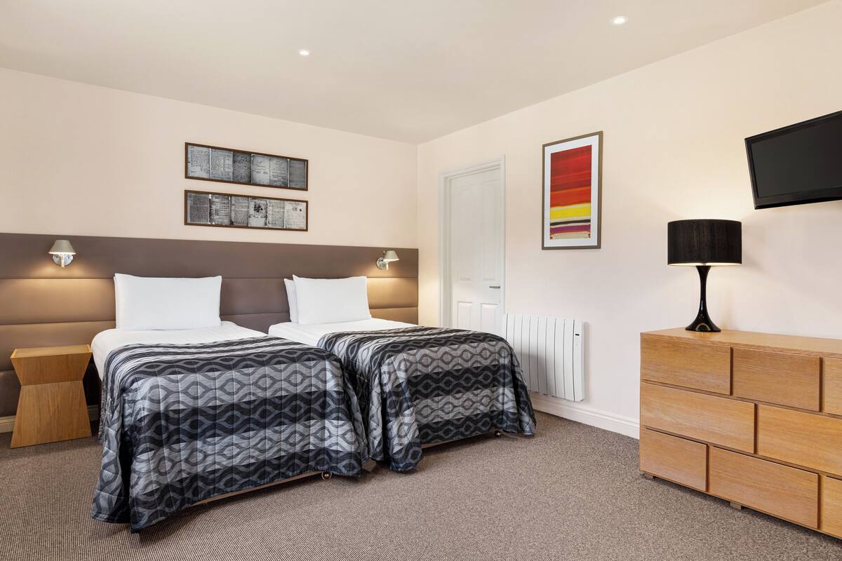 A hotel room with two beds, a wooden dresser, a flat-screen TV, and wall-mounted artwork.