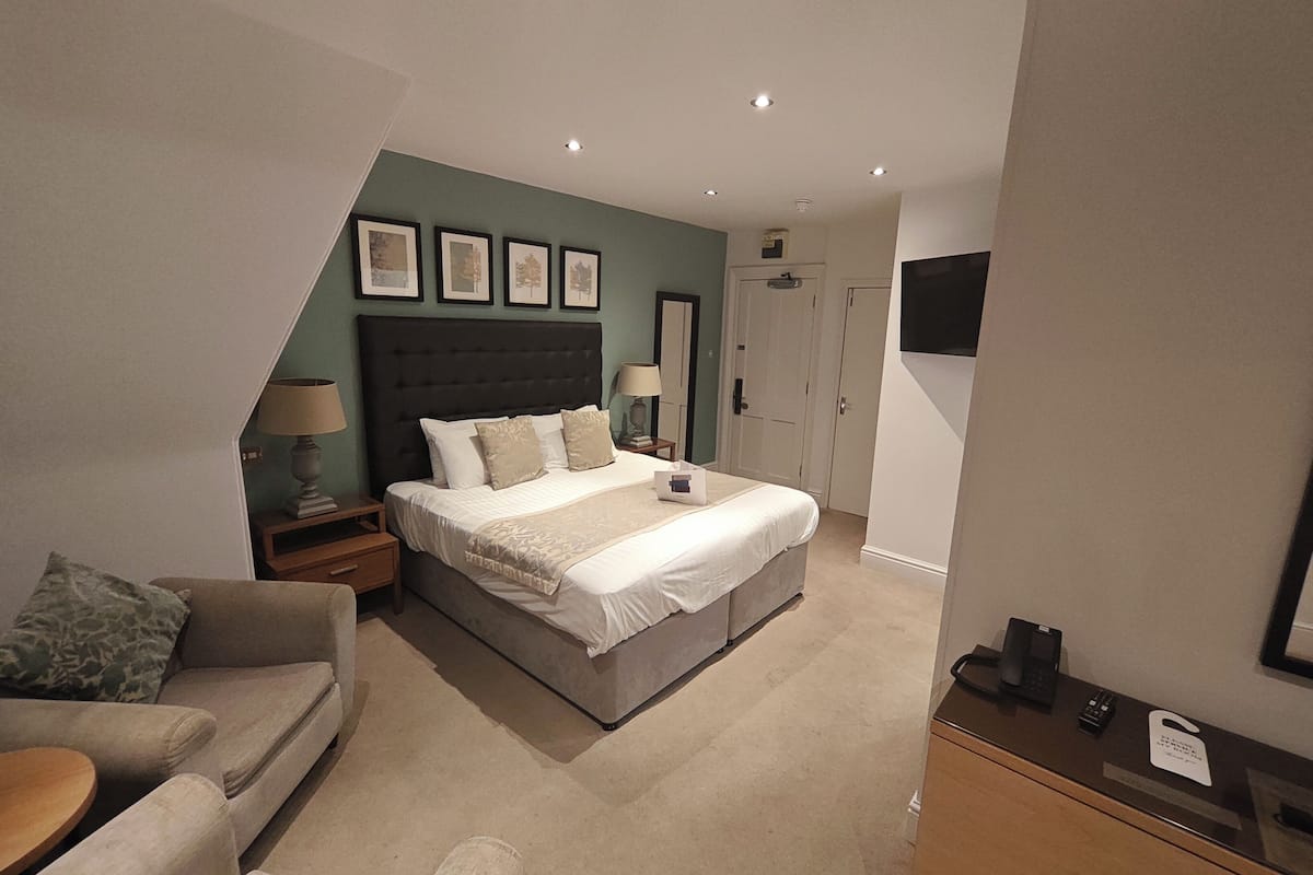 A modern hotel room with a large bed, a sofa, a desk with a telephone, and a flat-screen TV mounted on the wall.