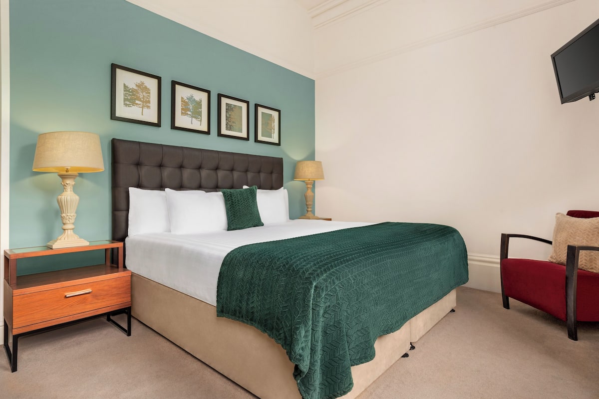A neatly arranged bedroom with a bed, two bedside tables, a chair, and framed pictures on the wall.