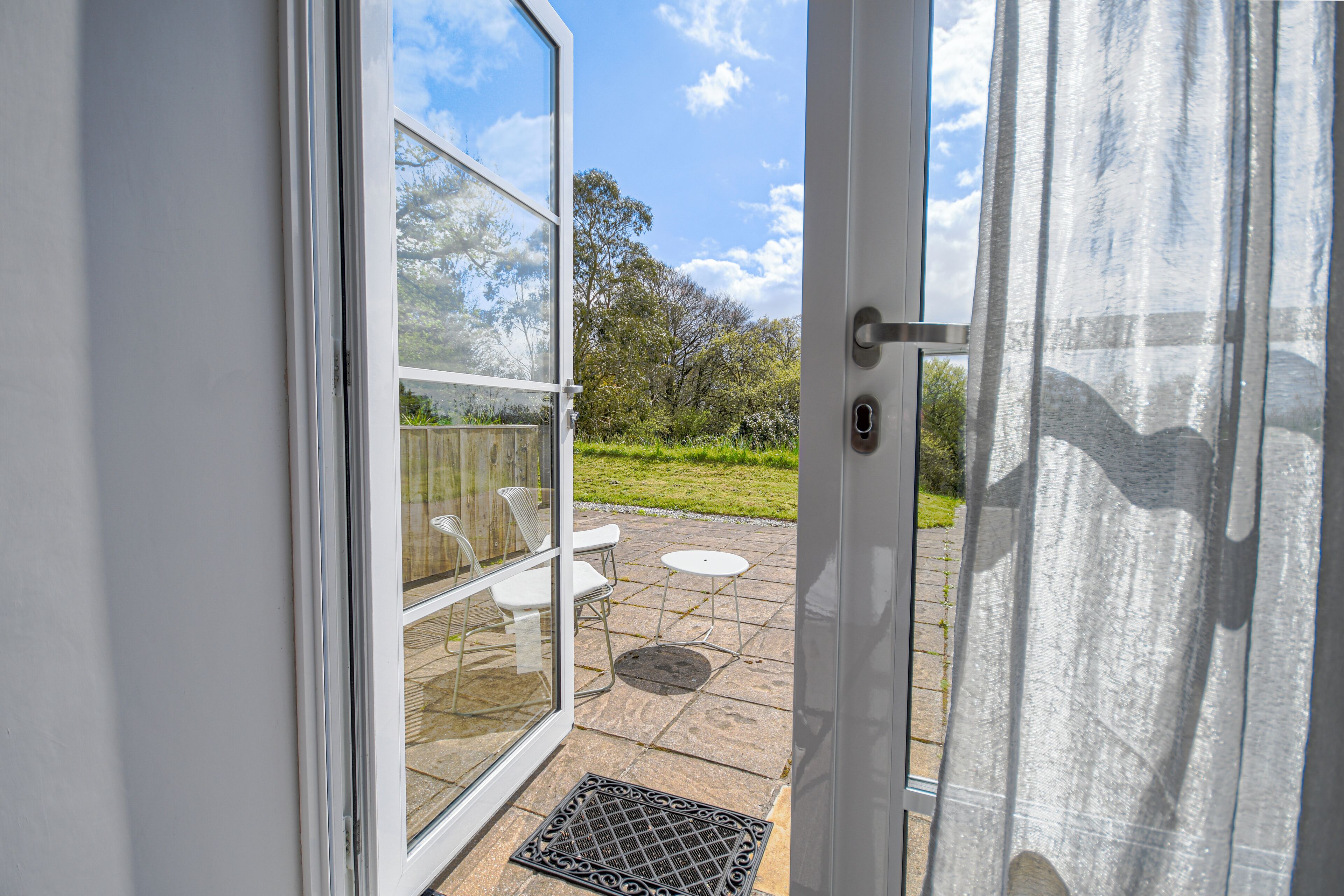 An open glass door leading to a patio with a white chair and a small table.