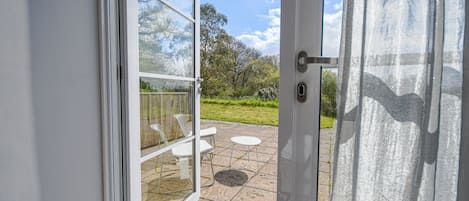 An open glass door leading to a patio with a white chair and a small table.