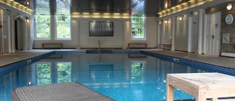 Une vaste piscine intérieure à l’eau d’un bleu limpide, entourée d’un haut plafond et de grandes fenêtres.