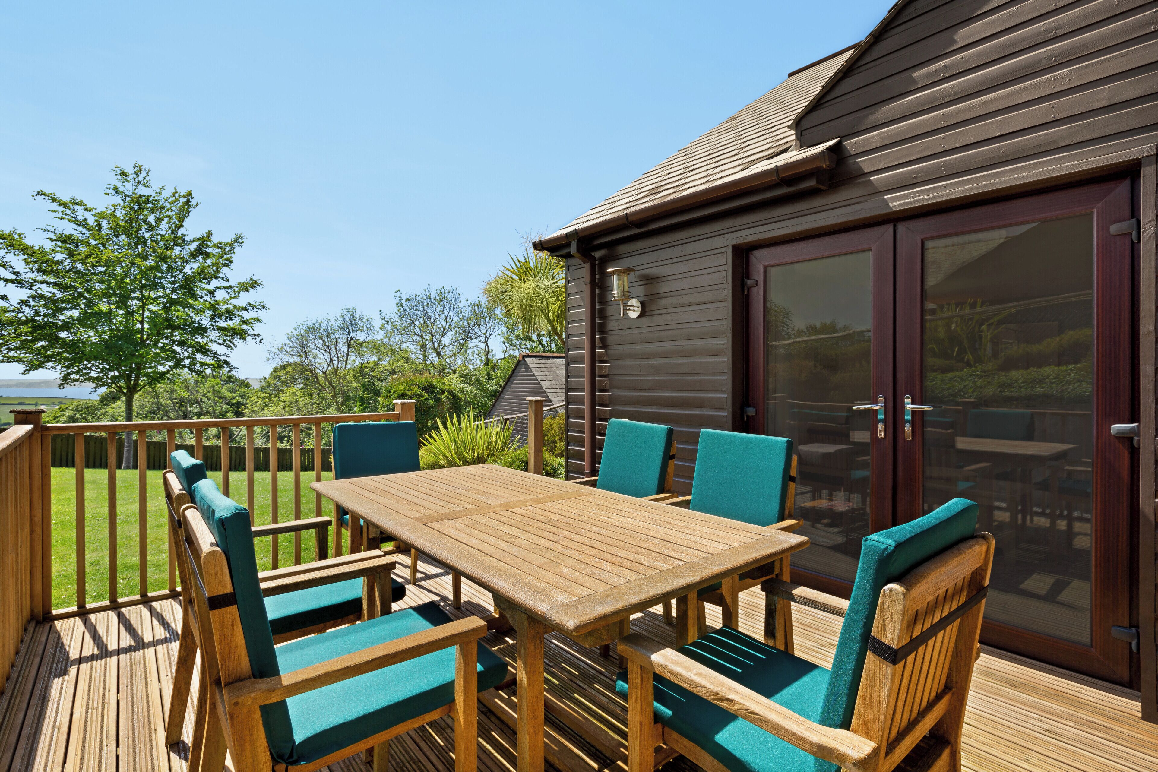 Um deck de madeira com mesa e cadeiras, uma porta de correr de vidro e vista para o exterior.