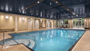 An indoor swimming pool with clear glass walls, a tiled floor, and a bench along the side.