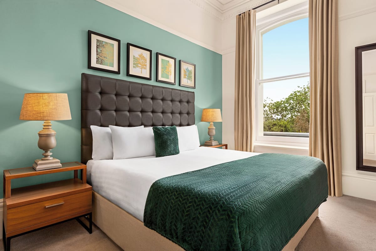A neatly made bed with a dark headboard, two bedside tables with lamps, and a window with curtains.