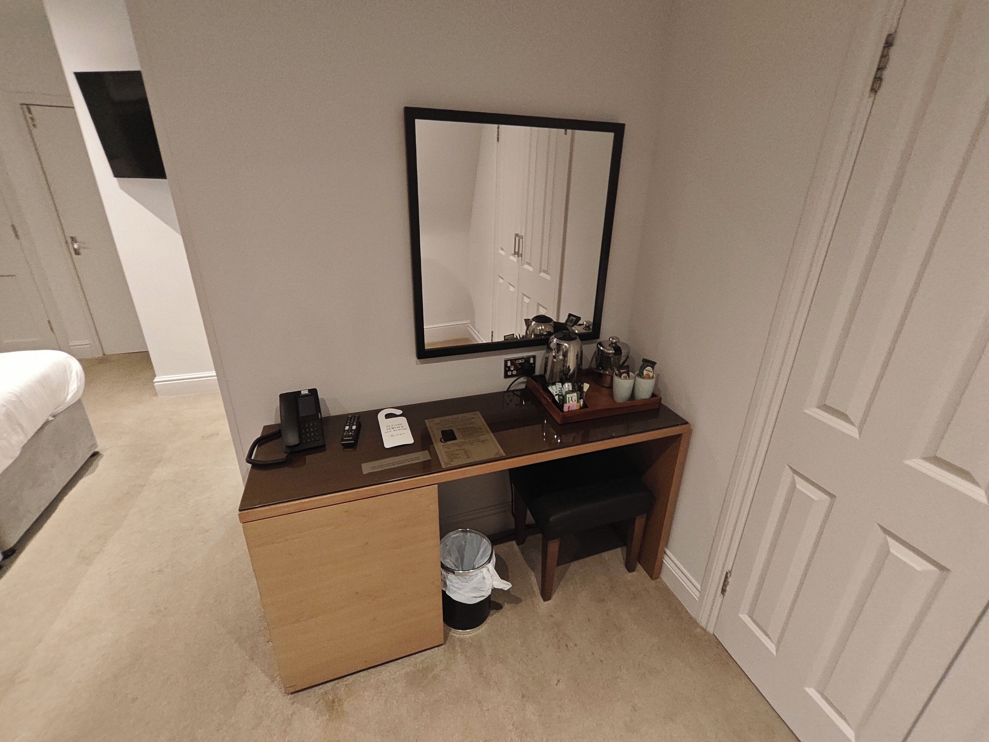 Habitación de hotel compacta con escritorio de madera, espejo, teléfono, cubo de basura y cama.