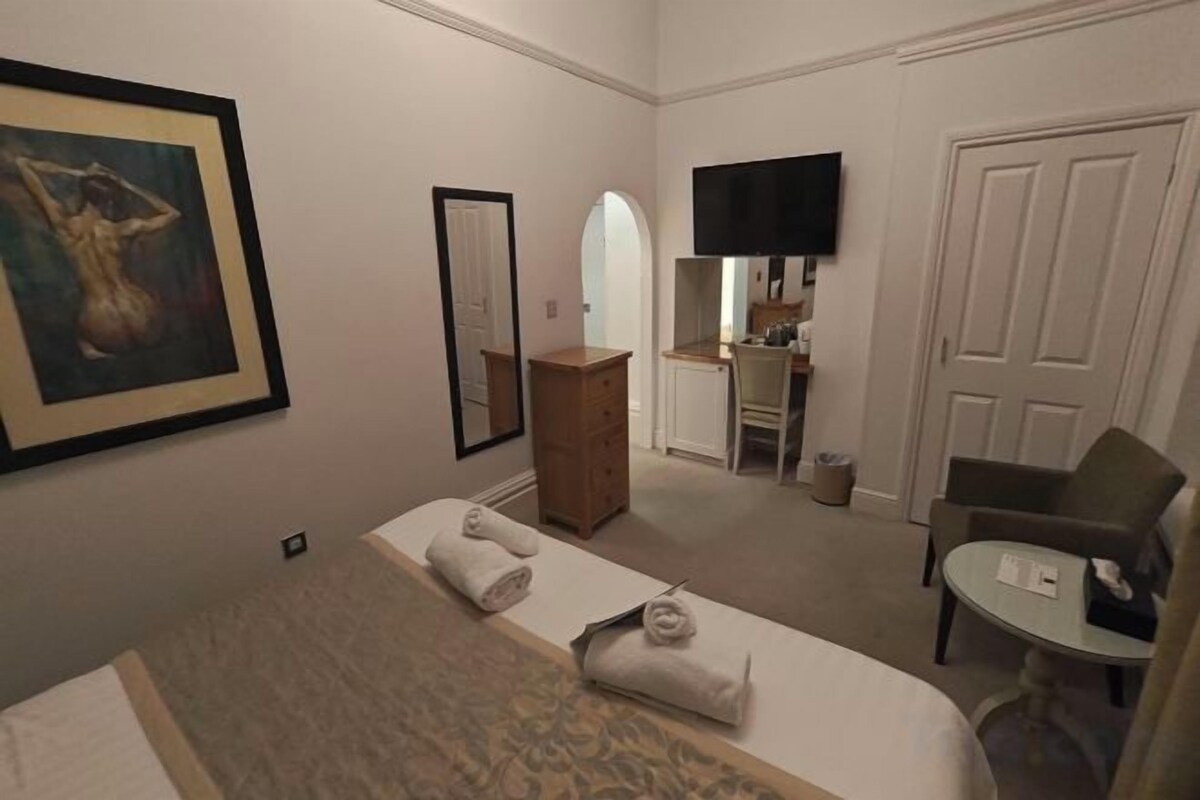 Ein Hotelzimmer mit Bett, Schreibtisch, Stuhl, Fernseher und einem Gemälde an der Wand.