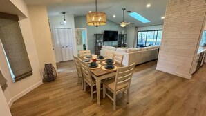 Un comedor amplio con una mesa de madera dispuesta para seis personas, rodeada de sillas. Un gran candelabro tejido cuelga sobre la mesa.