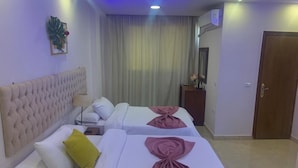 Una habitación de hotel con una cama grande, cabecera, mesita de noche, lámpara y cortina.