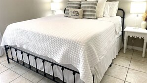 A neatly made bed with a white quilt, a black metal headboard, and two bedside tables with lamps.