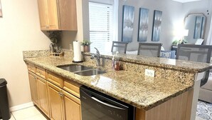 A kitchen with granite countertops, a dishwasher, wooden cabinets, and a window with blinds.