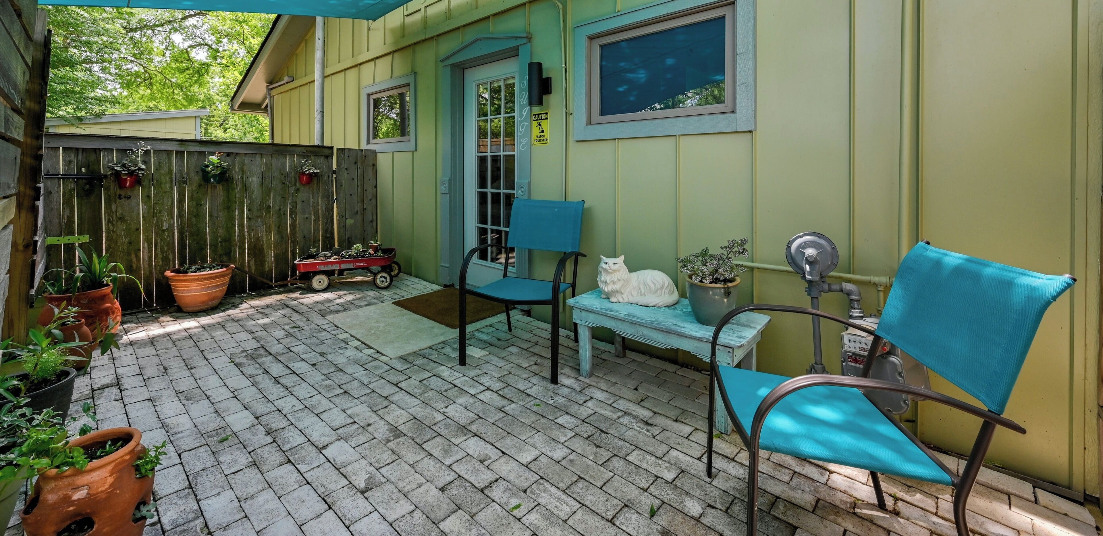 Eine Terrasse mit Holzzaun, Blumentöpfen, einer Bank und einer Katze.