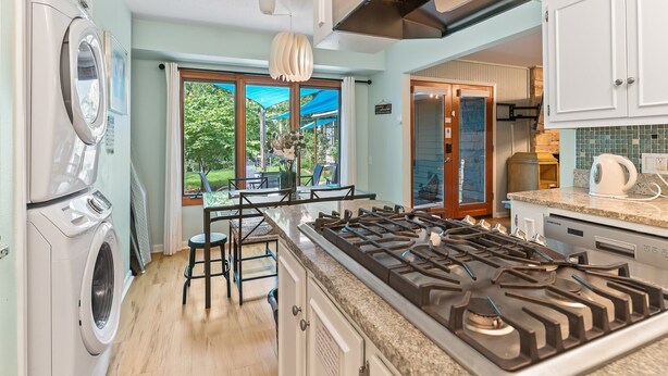 A modern kitchen with a built-in gas stove, a washing machine, and a dining area with a view of the outdoors.