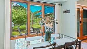 A dining area with a table and chairs, large windows with a view of greenery, and a sign on the wall.