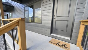 Una entrada de casa con una puerta gris, un porche de madera y un felpudo que dice 'hello'.