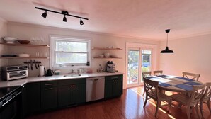 A kitchen with a central island, a dining table with chairs, and a view through the glass doors.