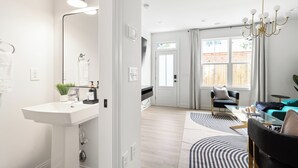 Een moderne, goed verlichte woonkamer met een groot raam, een kroonluchter en een bank.