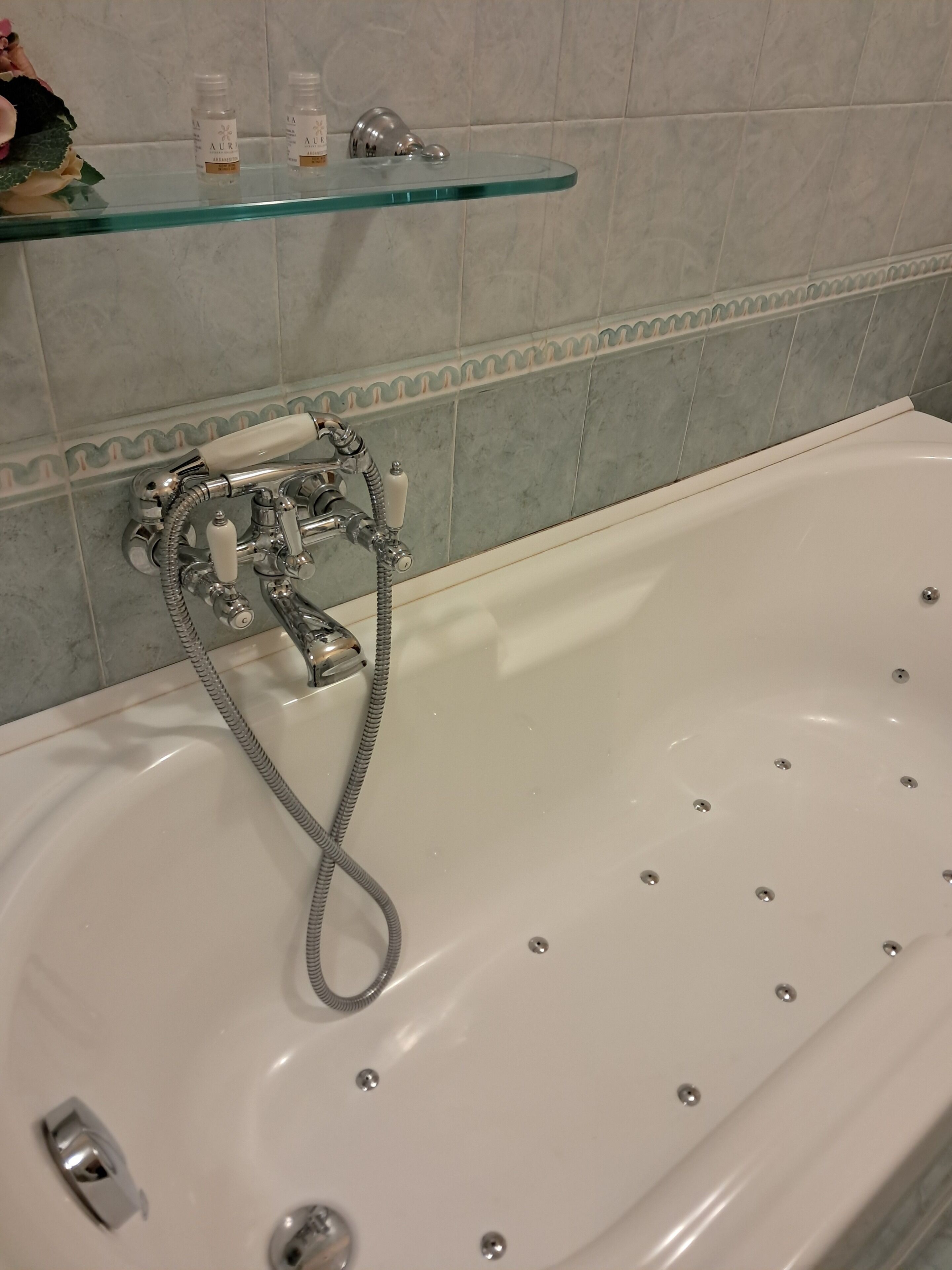 A bathroom with a white bathtub, a glass shelf with toiletries, and a shower with a chrome faucet.