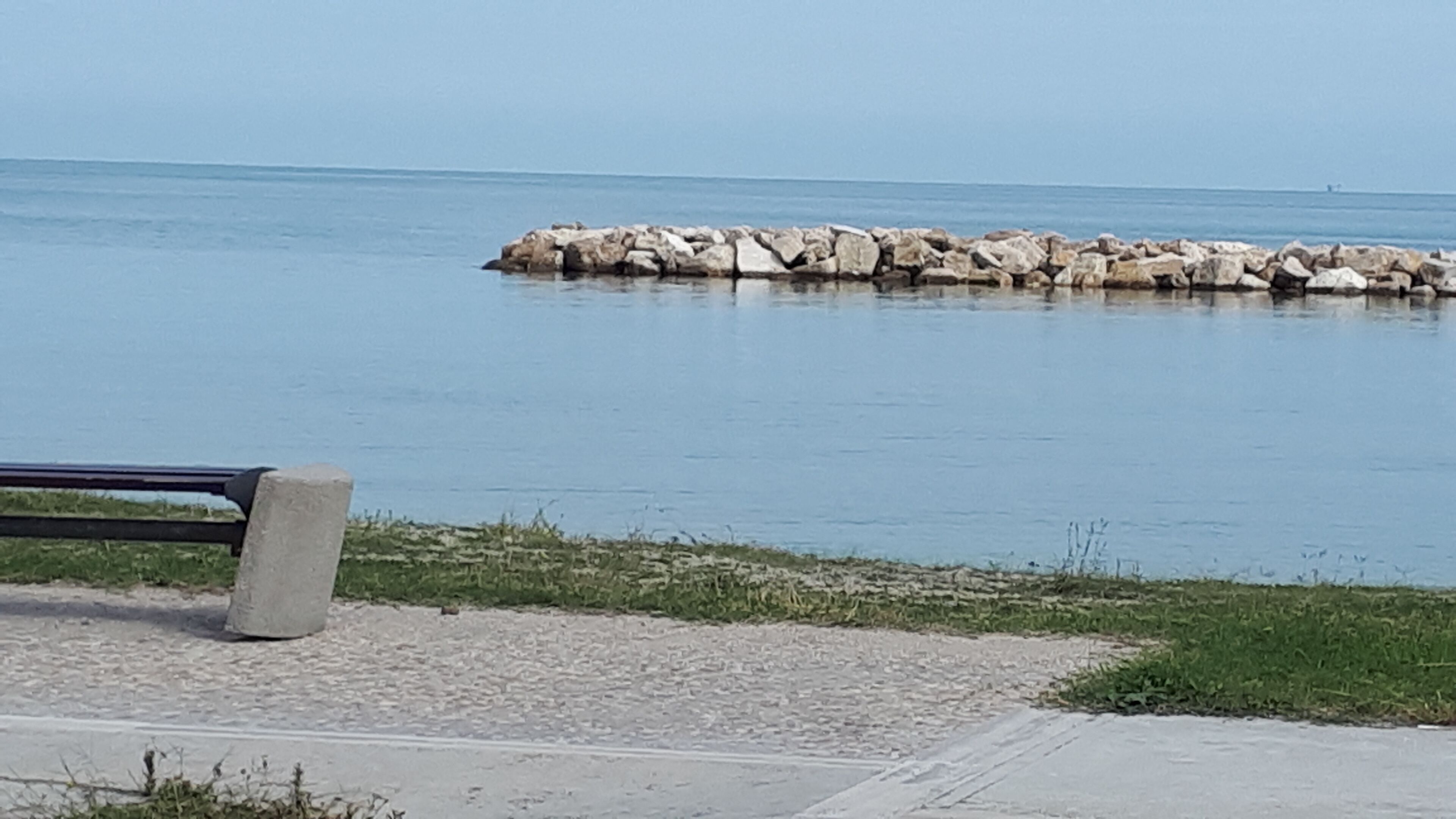 A bench by a rocky shoreline with calm water.