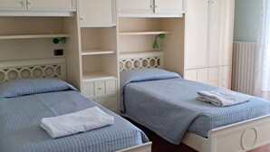 A bedroom with two single beds, white wardrobes, and a small desk with a lamp.