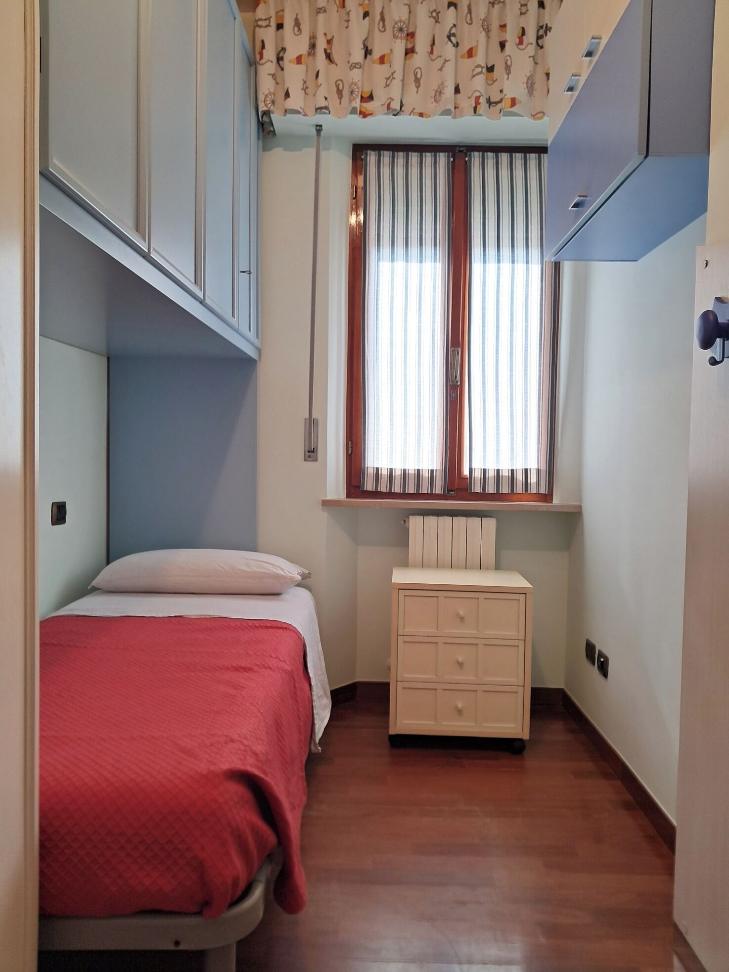 A bedroom with a bed, a dresser, a window with curtains, and a radiator.