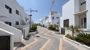 Un quartier résidentiel moderne avec des bâtiments blancs, un chemin sinueux et des grues de construction en arrière-plan.