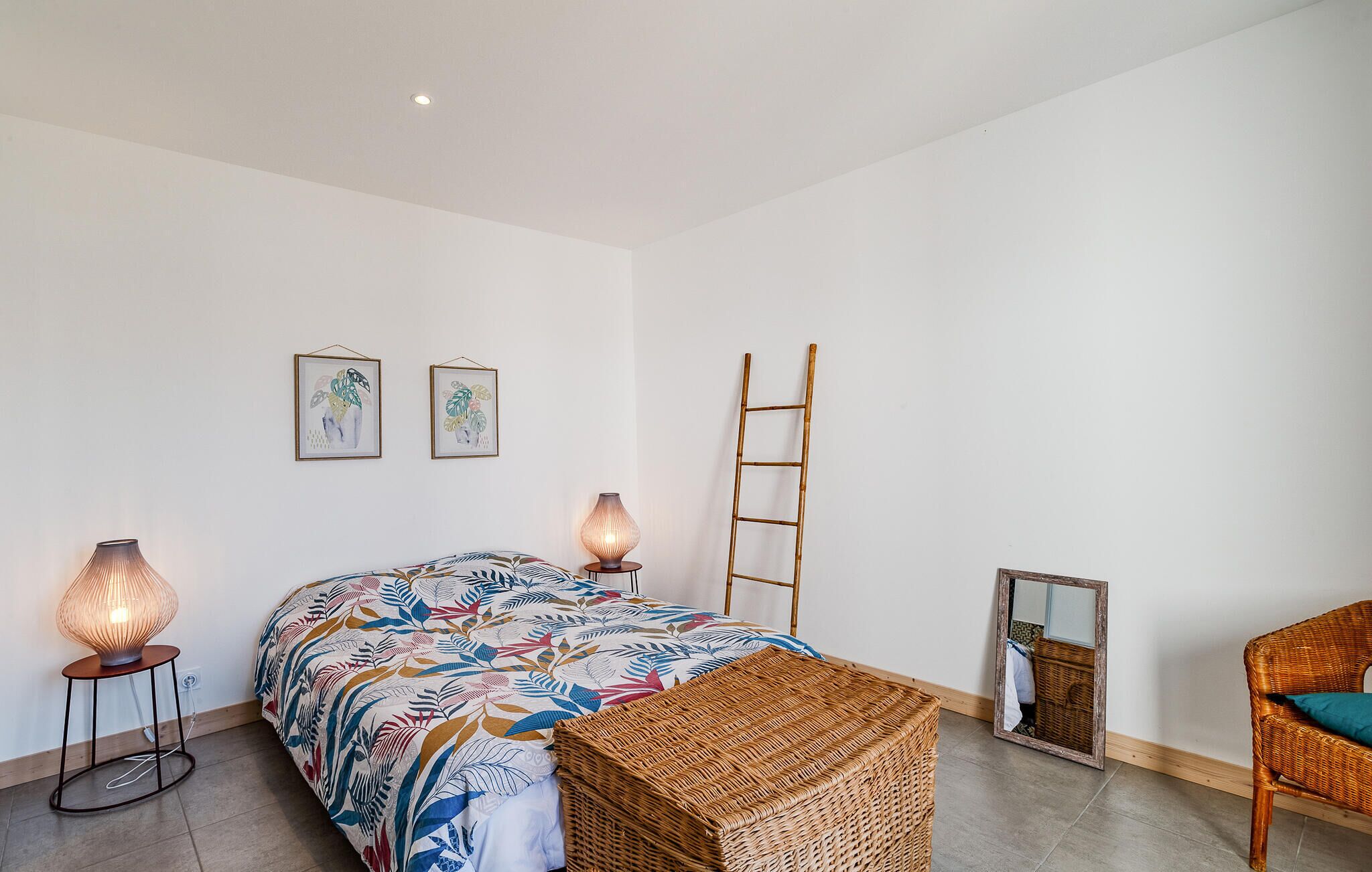 Une chambre à coucher avec un lit, deux lampes fixées au mur, un banc en osier, une échelle et un miroir.