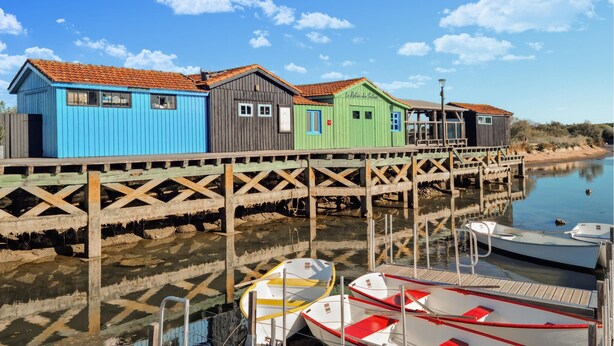 Un muelle de madera con edificios coloridos, un río tranquilo y barcos amarrados.