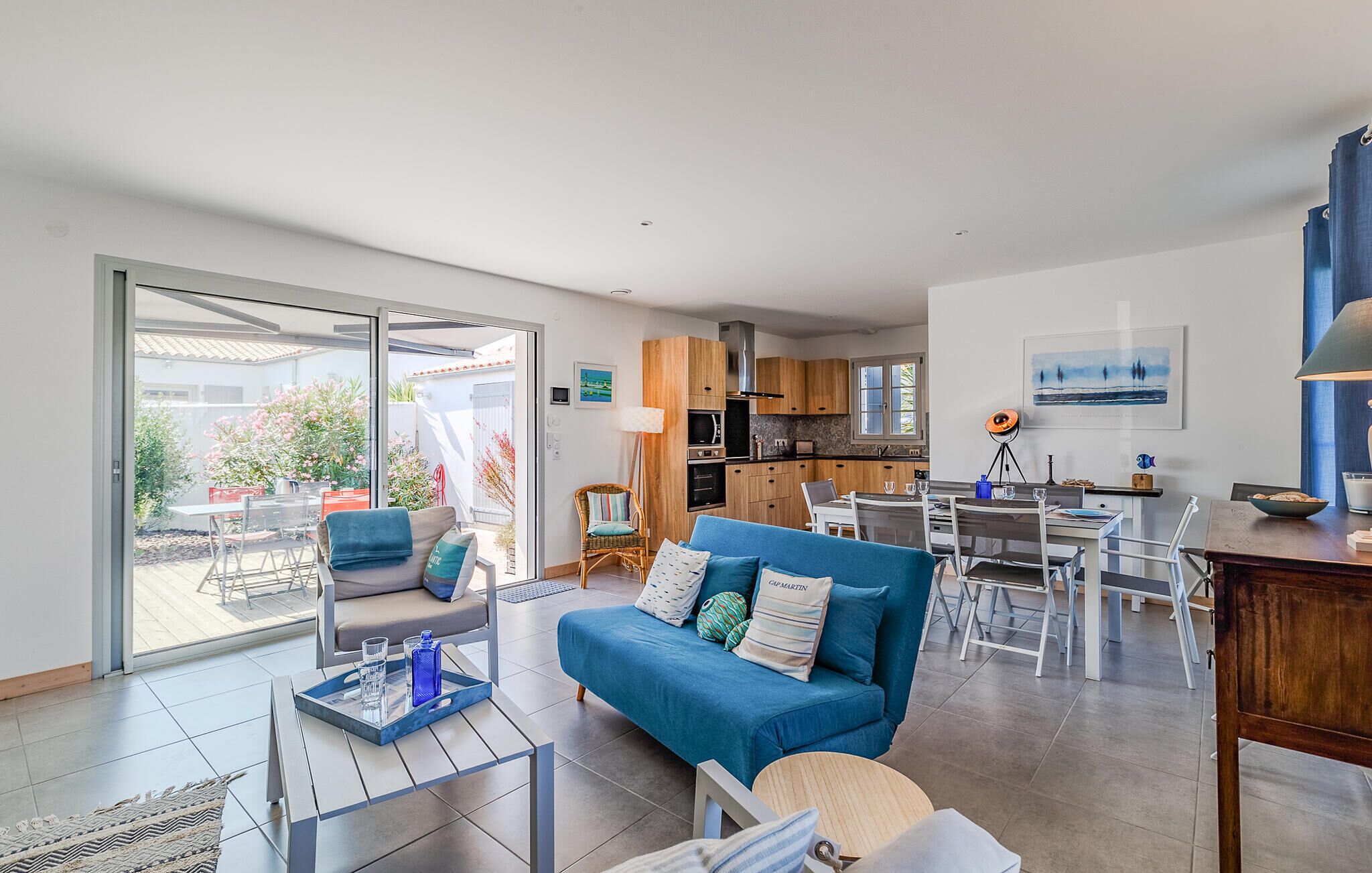 A modern living room with a blue sofa, a dining table, and a kitchen in the background.