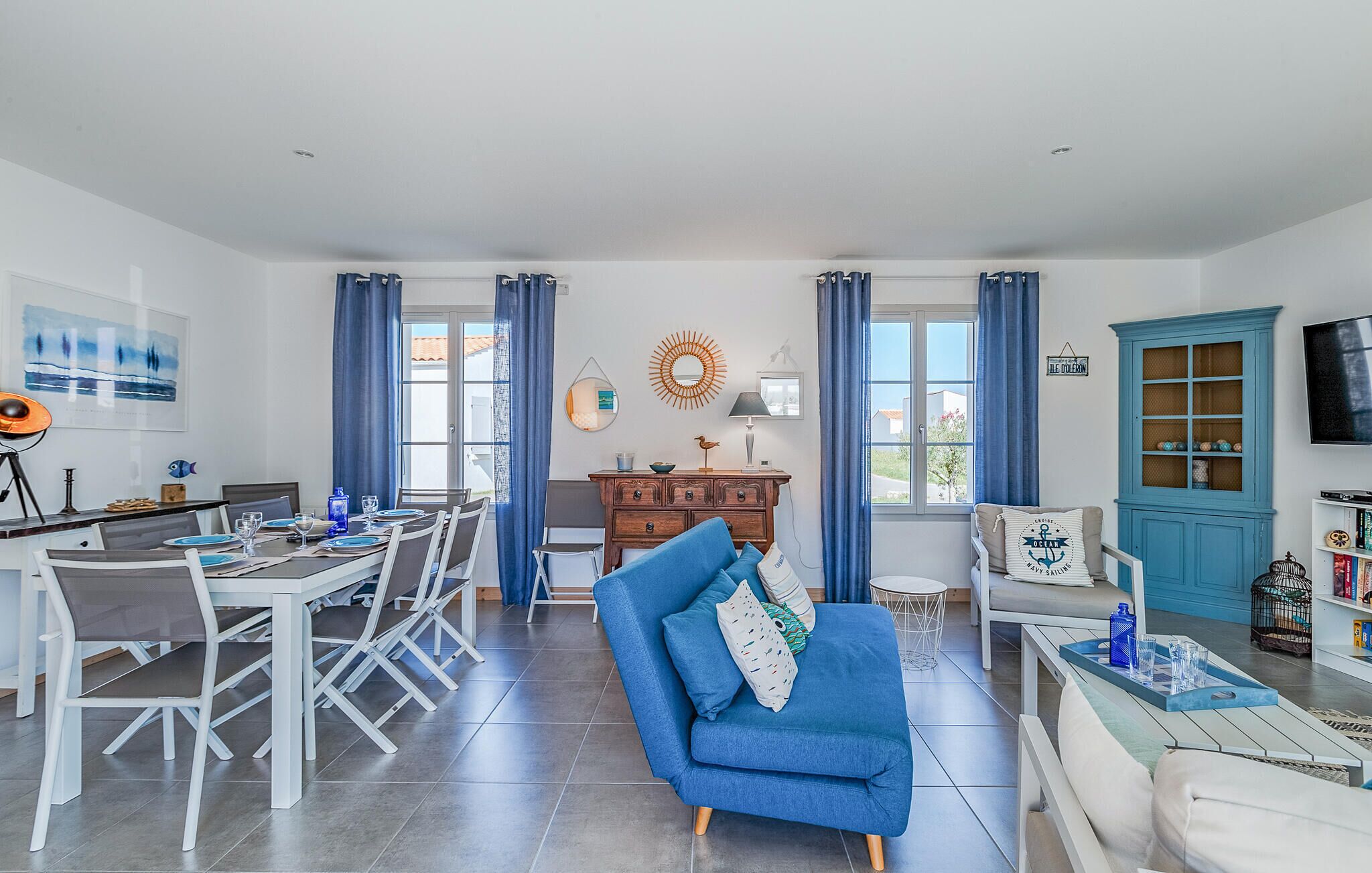 A bright living room with a dining area, a blue sofa, and a wooden cabinet.