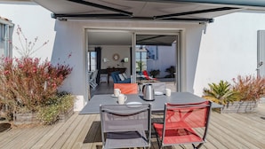 Un patio al aire libre con mesa y sillas, una zona cubierta y plantas en macetas.