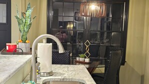 Una cocina con un lavamanos de acero inoxidable, encimera de mármol, una planta en maceta y una silla negra.