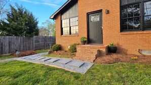 Una casa de ladrillo con puerta principal, ventanas y un pequeño jardín delantero con escalones y plantas en macetas.