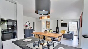 A modern kitchen with a central island, a dining area with a wooden table, and a living space with a sofa and a yellow chair.