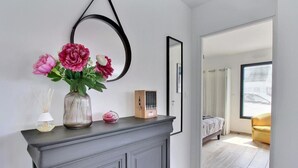 A modern room with a grey cabinet, a mirror, and a vase with flowers. There is a bed with a white headboard and a yellow chair in the background.