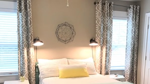 A bedroom with a bed, two bedside lamps, a nightstand, a ceiling fan, and a geometric wall decoration. - Above It All. Charming 2-bedroom apartment in the heart of Ocean Springs. (Ocean Springs)
