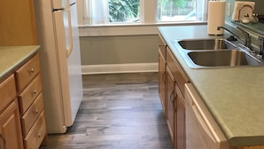 A kitchen with wooden cabinets, a refrigerator, a sink, and a window with a view of greenery. - Above It All. Charming 2-bedroom apartment in the heart of Ocean Springs. (Ocean Springs)