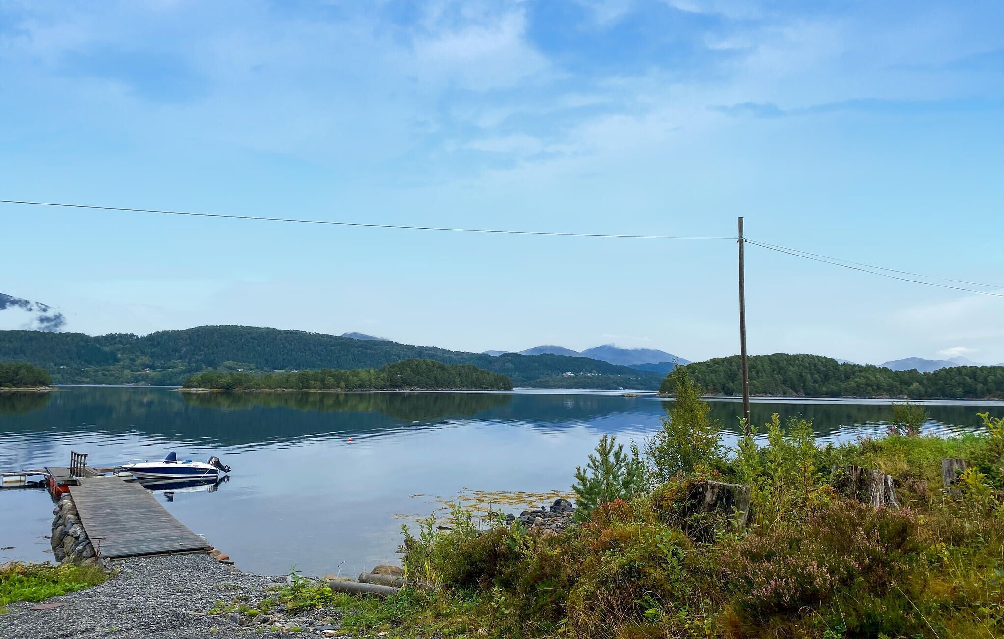 A calm lake with a dock, surrounded by greenery and mountains in the background.
